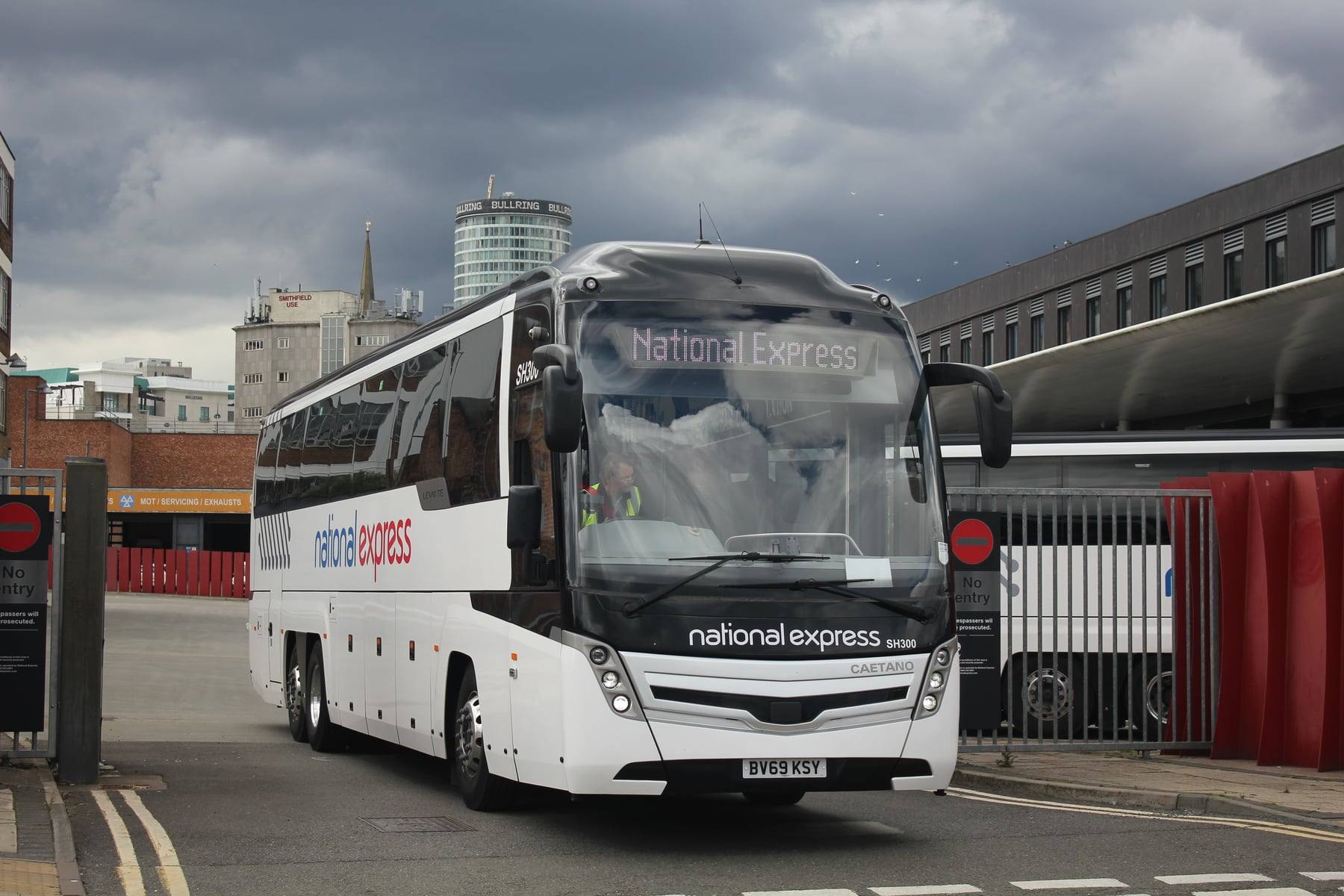 A white National Express coach to Birmingham Airport, with the Birmingham city skyline behind